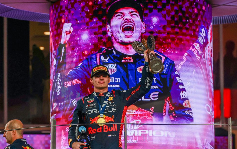 Makss Verstapens no Red Bull Racing uz goda pjedestāla ar savu trofeju pēc uzvaras Formula 1 Abū Dabī Grand Prix 2023. Avots: Imago Images